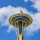 Space Needle observation tower in Seattle with American flag flying from top against blue sky with white clouds